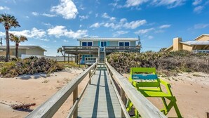 Una propiedad frente a la playa con un paseo marítimo de madera que conduce a un edificio de dos pisos con balcón.