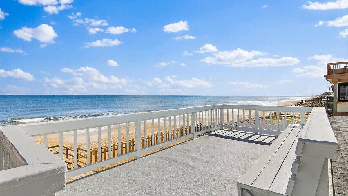 A beach view from a balcony with a railing, a sandy beach, and the ocean.