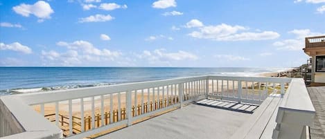 A beach view from a balcony with a railing, a sandy beach, and the ocean.