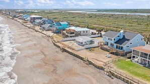 A coastal residential area with houses along the beach, a wooden boardwalk, and a view of the ocean.