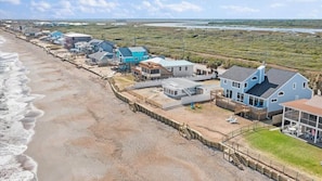 A coastal residential area with houses along the beach, a wooden boardwalk, and a view of the ocean.