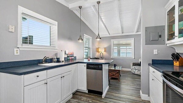 A kitchen with white cabinets, a dishwasher, a countertop, and pendant lighting.