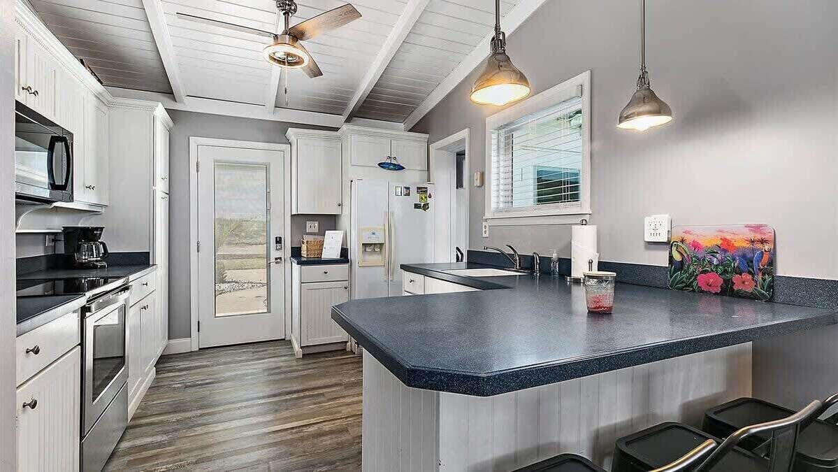 A kitchen with white cabinets, a black countertop, a ceiling fan, and a window with blinds.