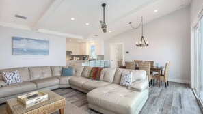 A spacious living room with a large L-shaped sectional sofa, a dining area with a table and chairs, and a kitchen in the background.