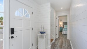 A hallway with white paneled walls, a door with a small window, and a blue shelf with a decorative item. - Sandy Toes Home with Hot Tub & Dune Deck (Ponte Vedra Beach)