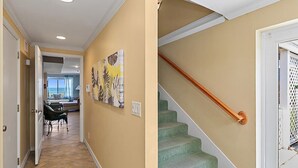 Un pasillo con una escalera, una puerta y vista a una sala de estar con un sofá y una mesa.