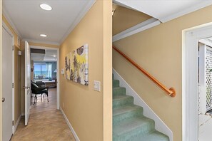 A hallway with a staircase, a door, and a view into a living area with a sofa and a table. - Seaside Sanctuary Home, Studio & Beach Walkout (St. Augustine)