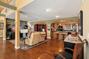 Amplia sala de estar con sofá, comedor con mesa y cocina con alacenas de madera y una barra.