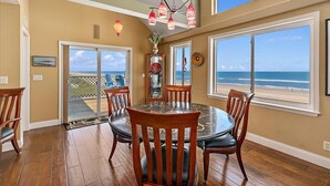 A dining area with a large table and chairs, a view of the ocean through large windows, and a ceiling with a unique light fixture.