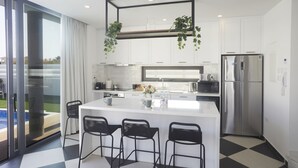 Una cocina moderna con una isla central, taburetes de bar y un refrigerador de acero inoxidable.