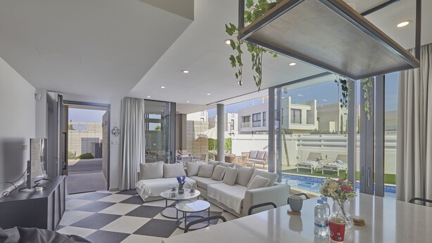 Una habitación de hotel moderna con suelo a cuadros, un sofá, una mesa de centro y vistas a la piscina y edificios cercanos.