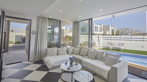 Una sala de estar moderna con un sofá grande, una mesa de centro y vistas a una piscina y edificios.