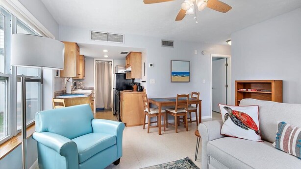 A modern living room with a blue sofa, a grey sofa, a dining area with wooden chairs, and a kitchen with wooden cabinets. - Courtyard Home with Fire Pit & Fenced Backyard (St. Augustine)