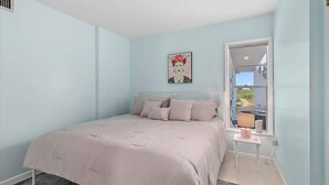 A bedroom with a bed, a window, a bedside table, and a wall-mounted artwork. - Courtyard Home with Fire Pit & Fenced Backyard (St. Augustine)
