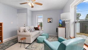 A living room with a sofa, ottomans, a coffee table, a TV, and a ceiling fan.
