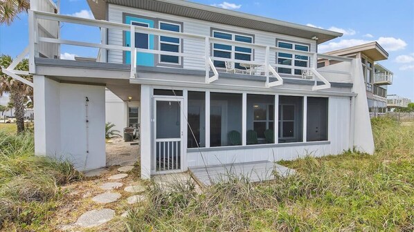 A coastal house with a balcony, large windows, and a stone pathway leading to the entrance.