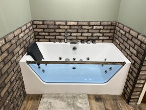A modern bathroom with a freestanding bathtub, a wooden floor, and a brick accent wall.