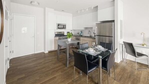 Une cuisine moderne avec des meubles blancs, des appareils en acier inoxydable et un coin repas comprenant une table en verre et des chaises noires.