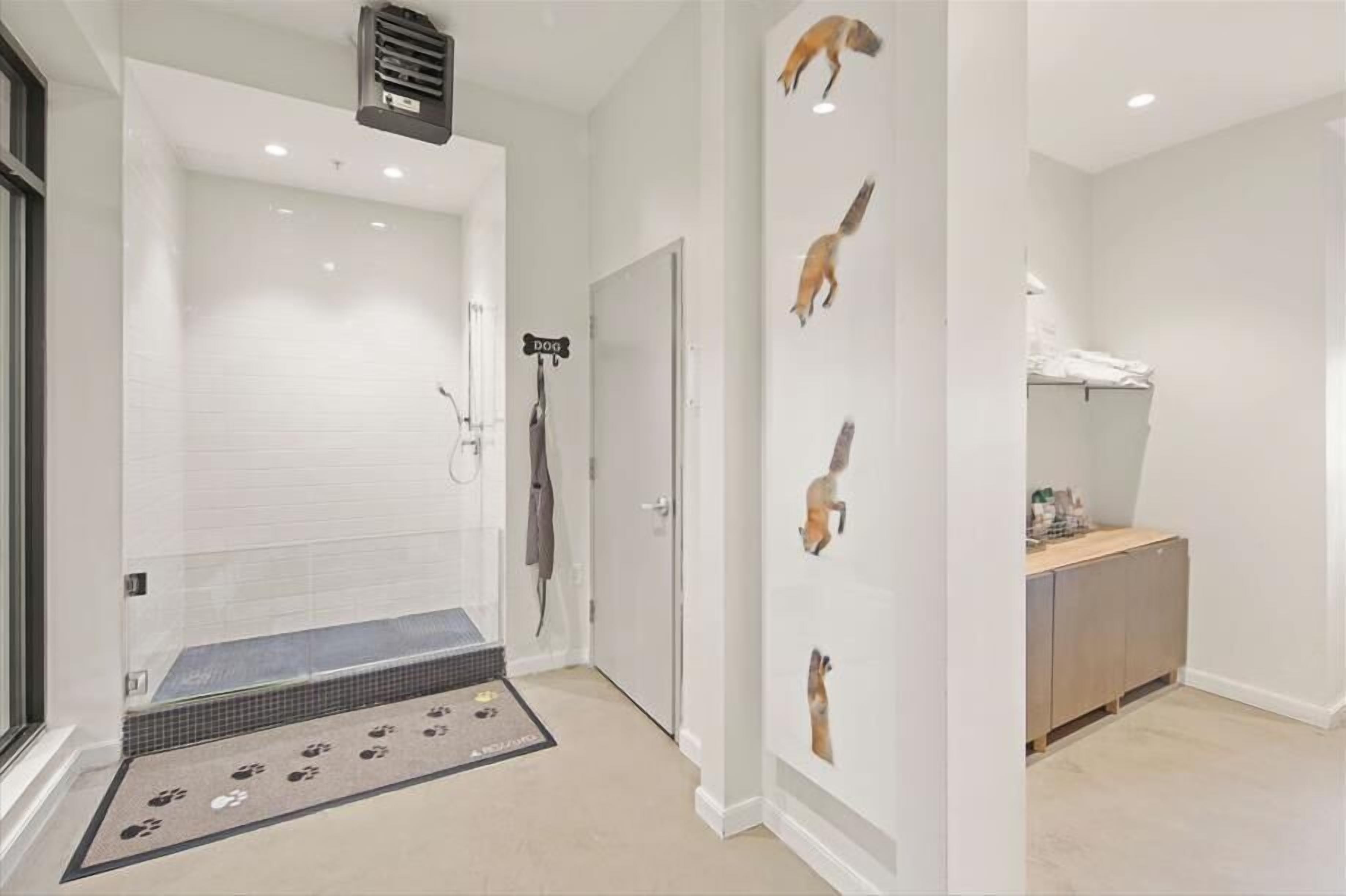 A modern bathroom with a glass shower enclosure, a dog-themed wall decoration, and a small wooden vanity.