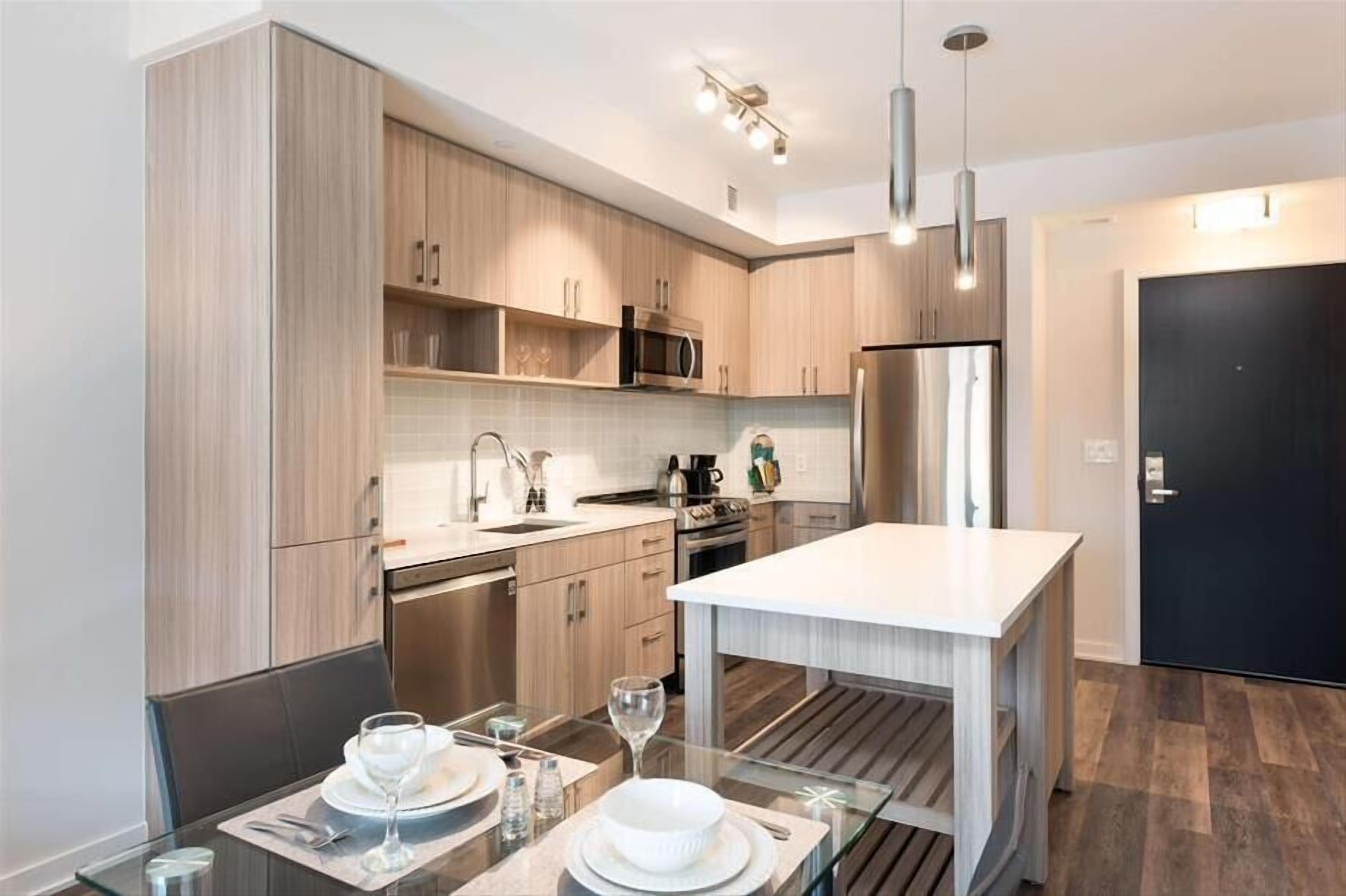 A modern kitchen with wooden cabinets, stainless steel appliances, and a dining area with a glass table.