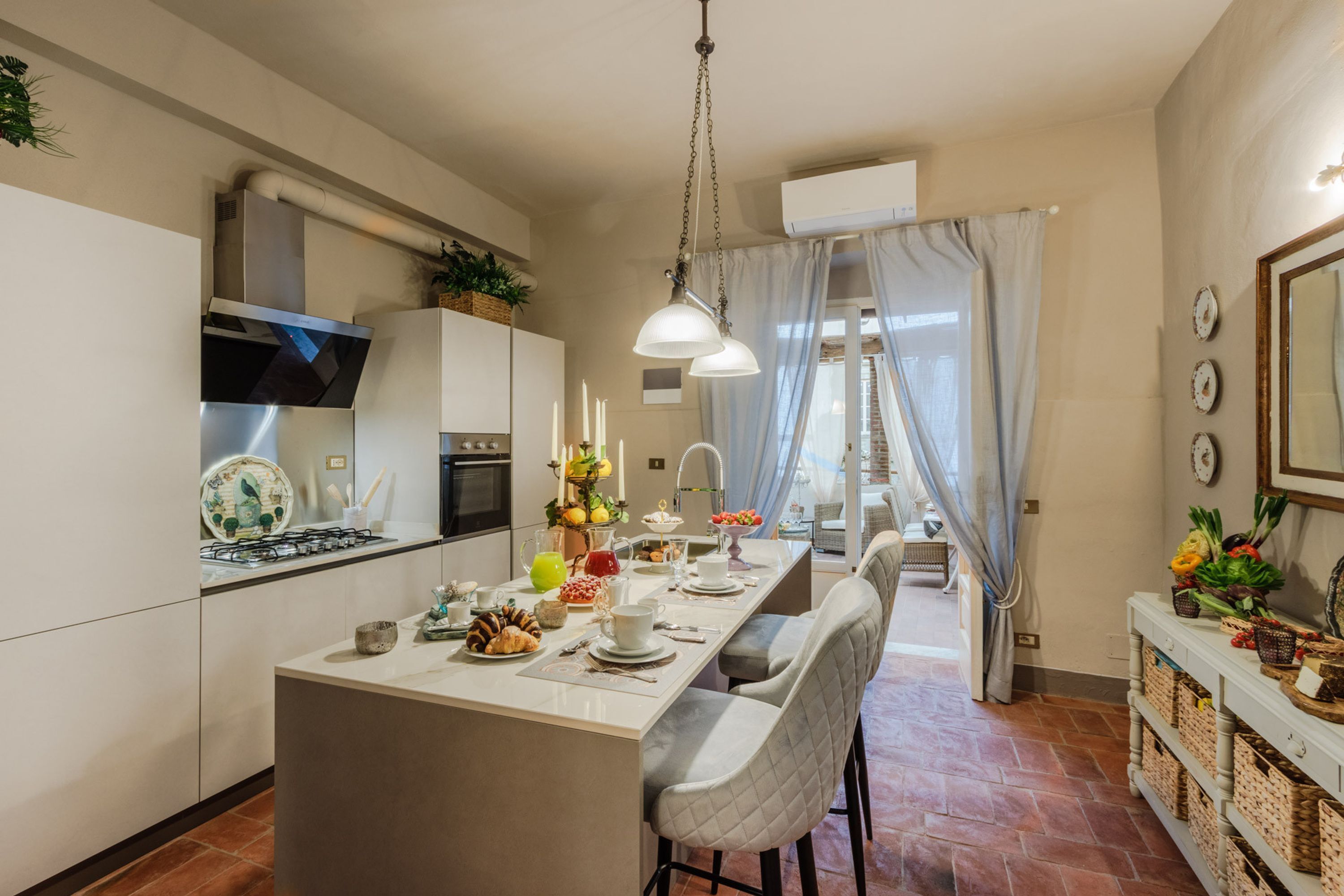A modern kitchen with a central island, a dining area with bar stools, and a view of the outdoors through a large window.
