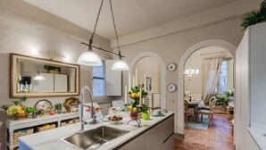 A modern kitchen with a large island, stainless steel sink, and pendant lighting. There are various kitchen items and decorations on the counter. - Casa Celeste With Terrace (Lucca)