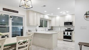 A modern kitchen with white cabinetry, a central island, and a dining area with chairs. - 5 Bedroom 3 Bath in Northwest SA (San Antonio)
