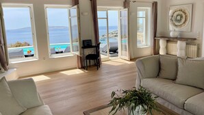 Ein geräumiges Wohnzimmer mit einer großen Couch, einem Couchtisch und Meerblick durch offene Fenster.