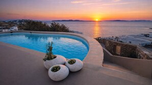 Ein Pool mit Blick auf den Sonnenuntergang, umgeben von weißen Gebäuden und einer Steinmauer.