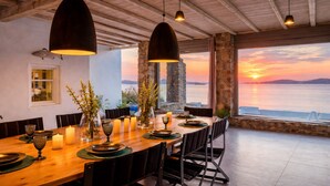 Ein Essbereich mit einem Holztisch, gedeckt für sechs Personen, großen Fenstern mit Sonnenuntergangsblick und Steinwänden.