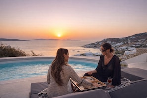 Two people playing a board game by a pool with a sunset view.