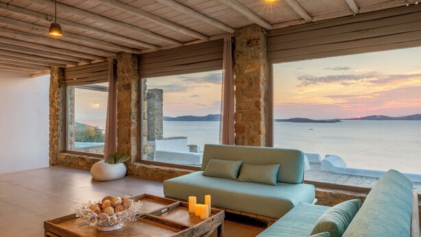 Ein geräumiges Zimmer mit Meerblick, ausgestattet mit einer Holzbalkendecke, großen Fenstern und einem grünen Sofa.