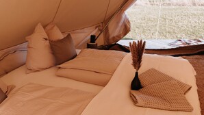 Een tent van binnen, met een bed, kussens, een deken en een decoratief object.