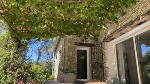 A stone building with a large glass door, a wicker table and chairs, and potted plants.
