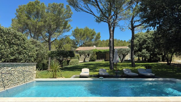 A swimming pool with lounge chairs, surrounded by a stone wall and trees.