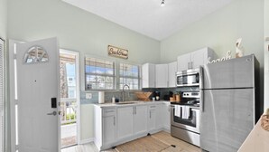 Een keuken met witte kasten, roestvrijstalen apparatuur en een bordje 'Beach House'.