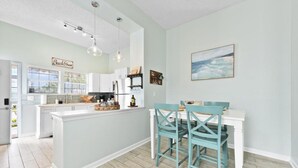 Een moderne keuken met witte kasten, een centraal eiland en teal-kleurige stoelen aan een eettafel.