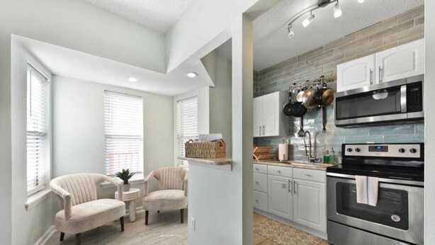 A modern kitchen with stainless steel appliances, light-colored cabinetry, and a small dining area with two chairs.