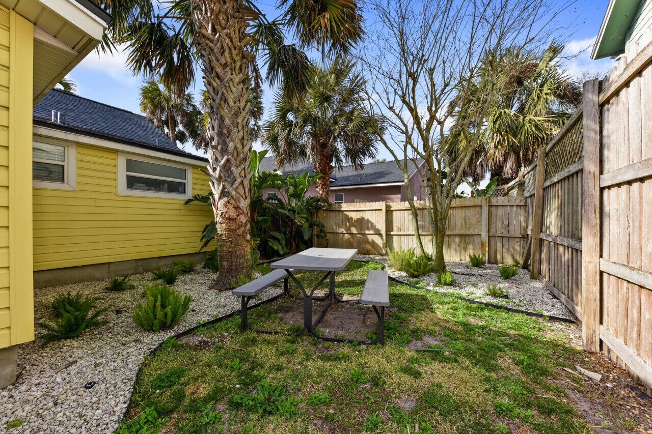A backyard with a picnic table, palm trees, and a wooden fence.