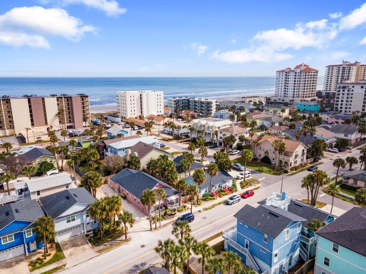 A coastal residential area with a mix of single-family homes and multi-story buildings, featuring a beach view.