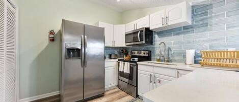 A modern kitchen with white cabinets, stainless steel appliances, and a blue-tiled backsplash.