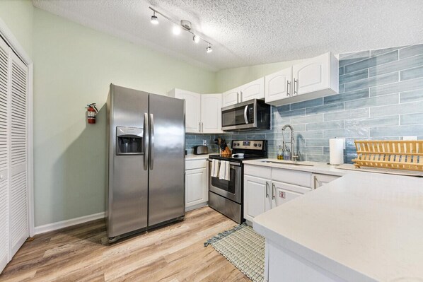 Una cocina moderna con gabinetes blancos, electrodomésticos de acero inoxidable y un respingo de azulejos azules.