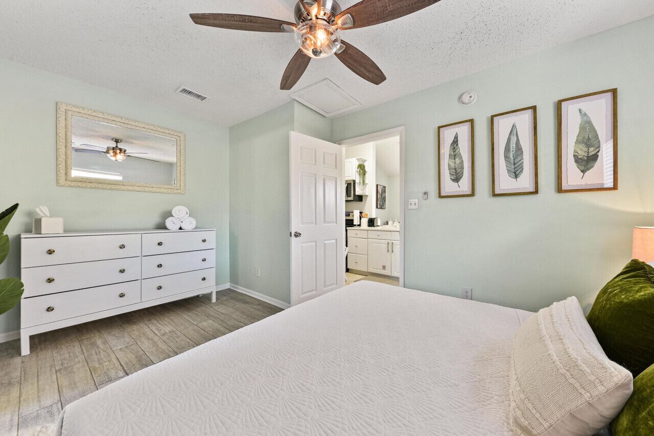 A bedroom with a bed, a dresser, a ceiling fan, a mirror, and framed leaf artwork on the wall.