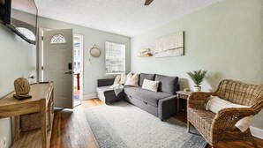Una sala de estar acogedora con un sofá seccional gris, un sillón de mimbre, una mesa de centro de madera y un ventilador de techo.