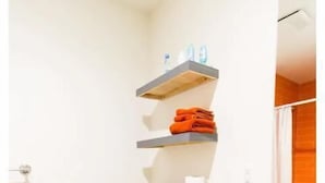 A compact bathroom with a white toilet, grey shelves, and a small trash bin. - Studio in the heart of Fishtown (Philadelphia)