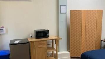 A compact hotel room with a bed, a small kitchenette with a microwave, a wooden cabinet, and a wardrobe.