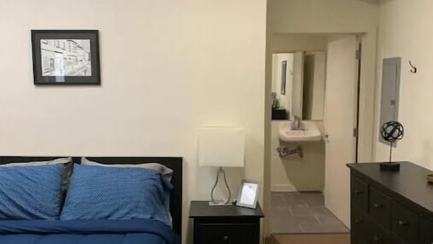 A bedroom with a bed, a nightstand, a dresser, and a framed picture on the wall. - Studio in the heart of Fishtown (Philadelphia)