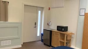 A room with a bed, a desk, a refrigerator, and an exit sign. - Studio in the heart of Fishtown (Philadelphia)
