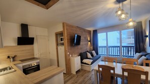 Eine moderne Küche mit Holzarbeitsplatte, Einbauofen und Mikrowelle. Es gibt einen Essbereich mit Holztisch und Stühlen, sowie eine Couch mit an der Wand montiertem Fernseher.