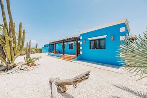 A modern house with a bright blue exterior, a covered patio, and a gravel driveway.